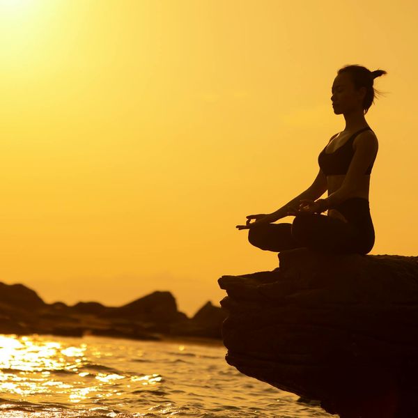 Silhouette of a person in a powerful yoga warrior pose at sunset.
